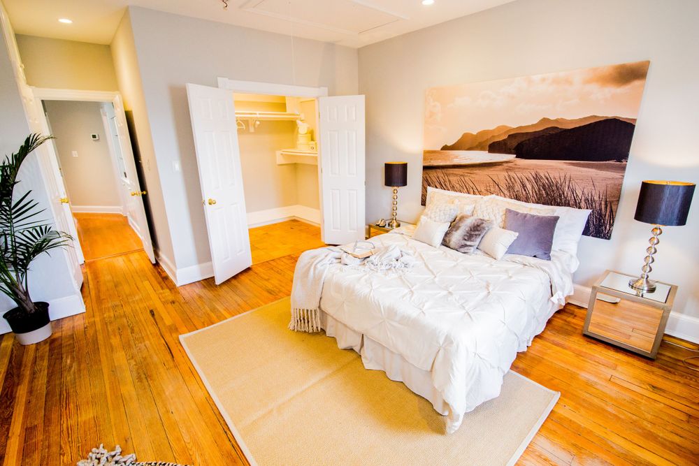 Spacious bedroom with hardwood floors, white bedding, and large closet space.