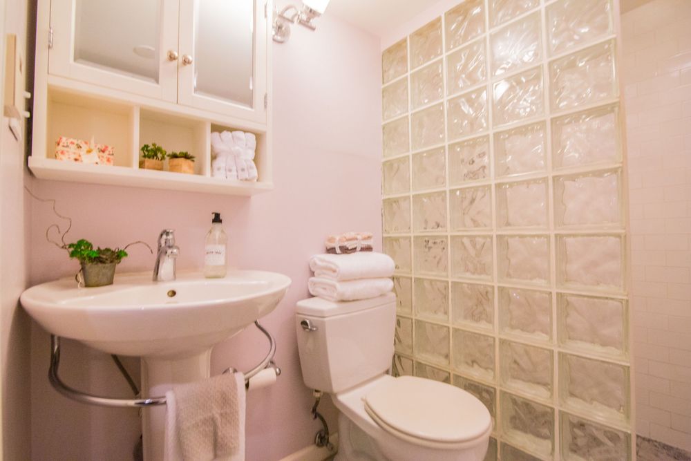 Clean white bathroom with glass block wall, pedestal sink, and built-in shelving.