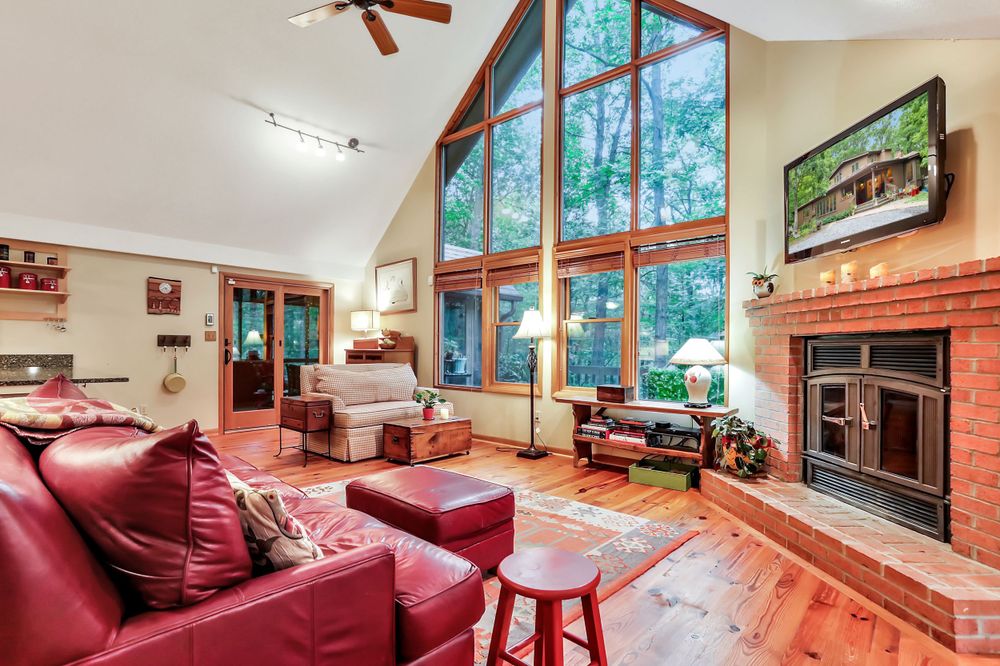 Cozy mountain cabin living room with vaulted ceiling, large windows, red couches and stone fireplace.