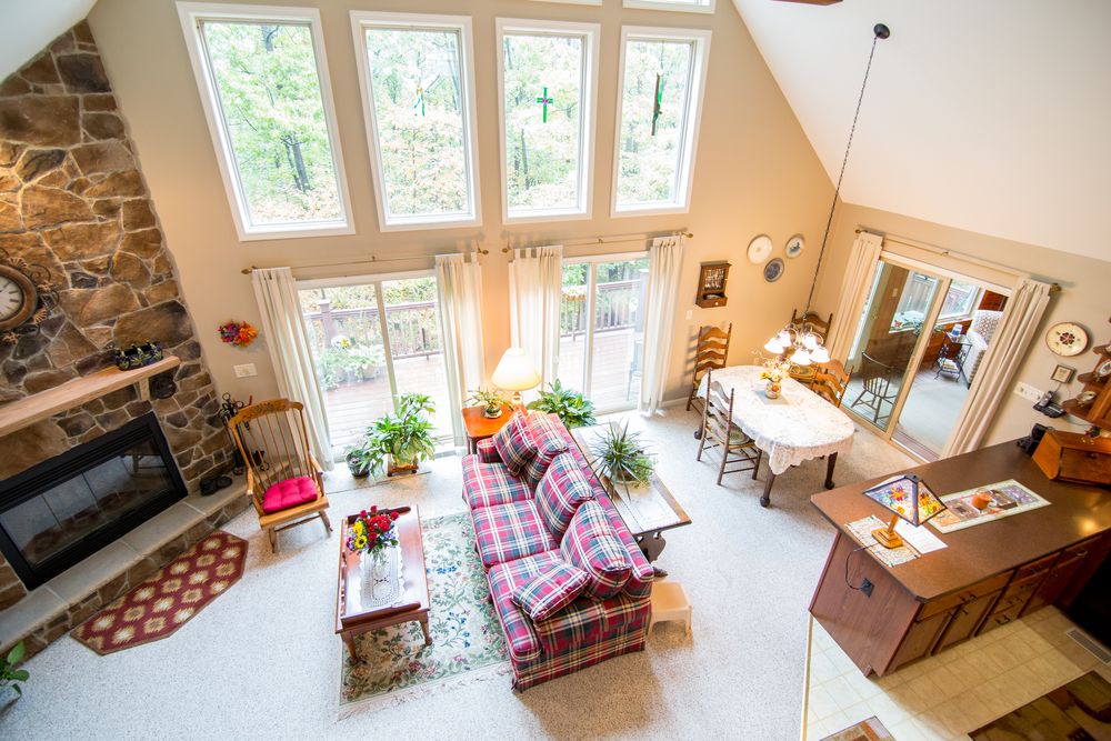 Cathedral ceiling great room with stone fireplace, plaid sofa, and abundant natural light.