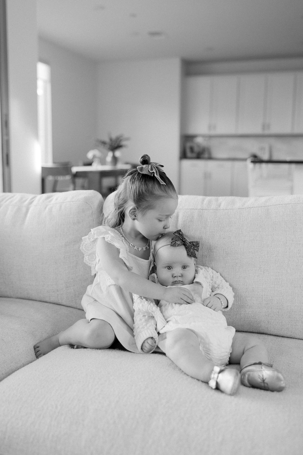 Black and white photo series showing tender moments between parent and baby on a light colored couch.
