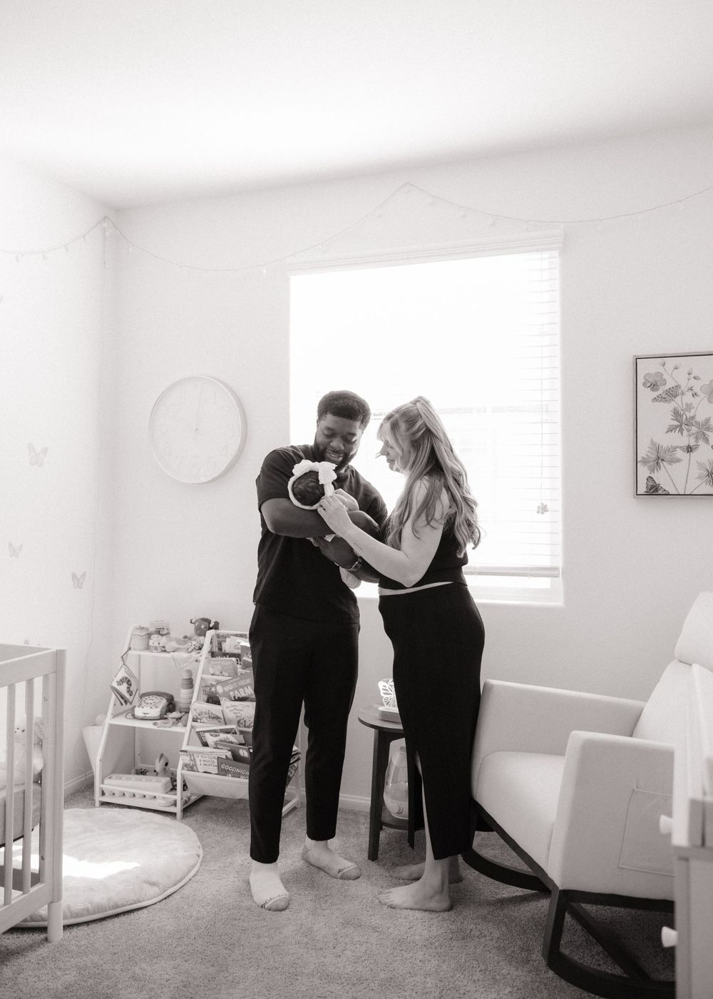 A couple holds up a small baby in a cozy nursery room with natural light.