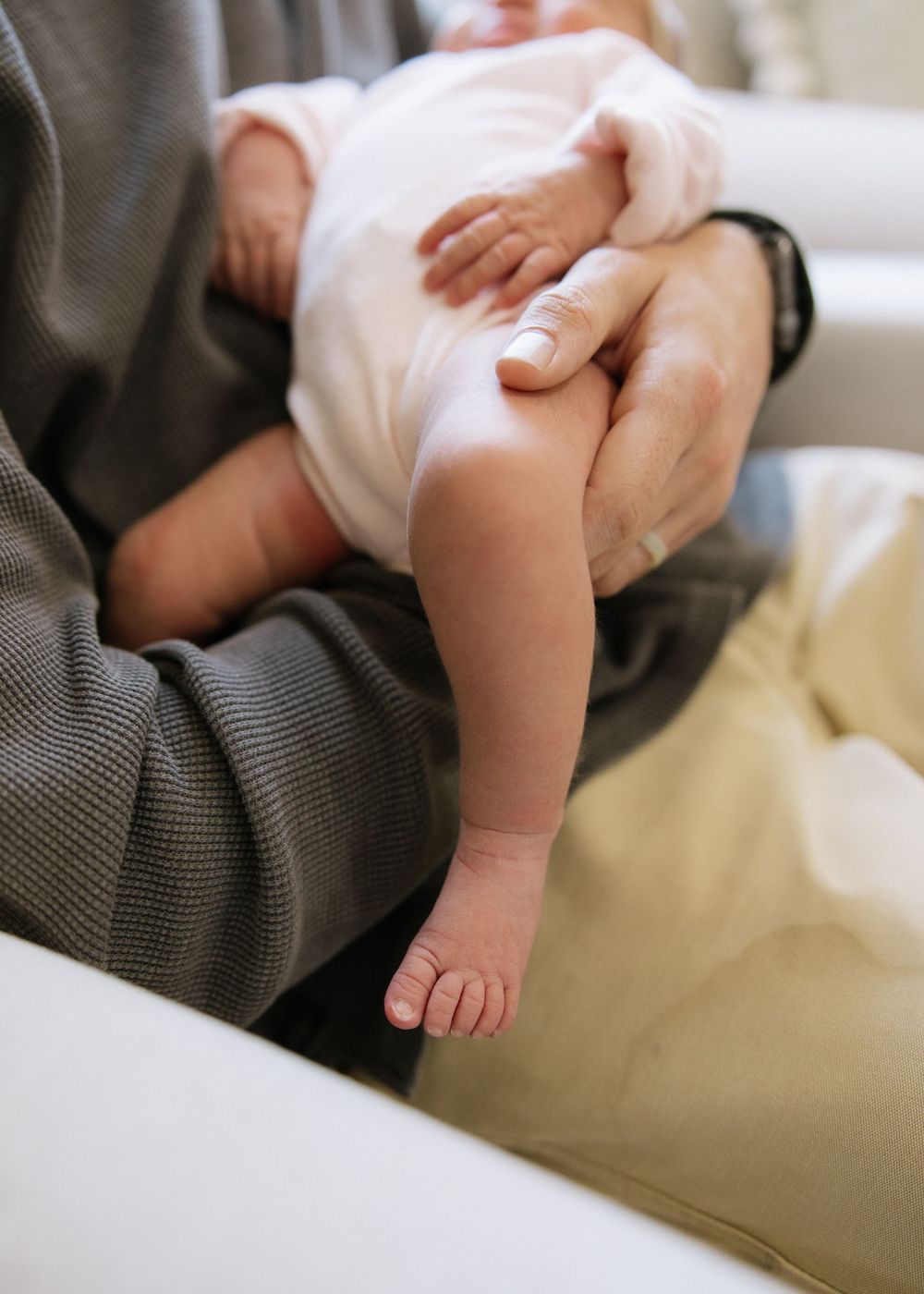 Close-up of tiny baby feet and legs being held gently in someone's hands.