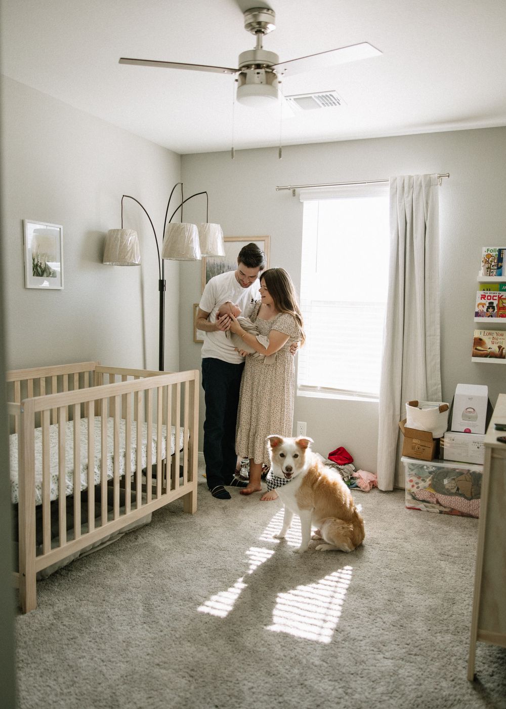 A couple embraces in a bright nursery room while their dog sits in a sunbeam.