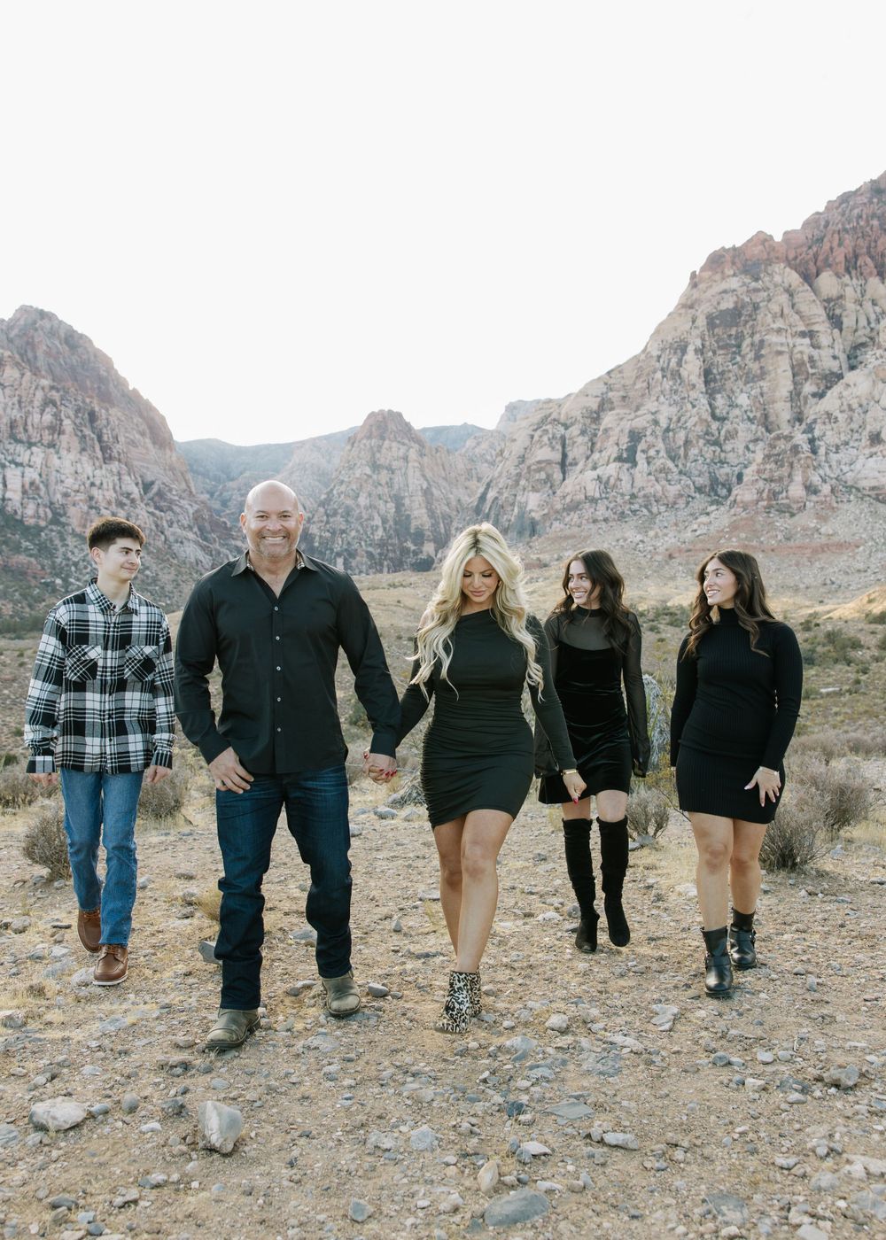 Group walking together in black outfits against a scenic desert mountain landscape.