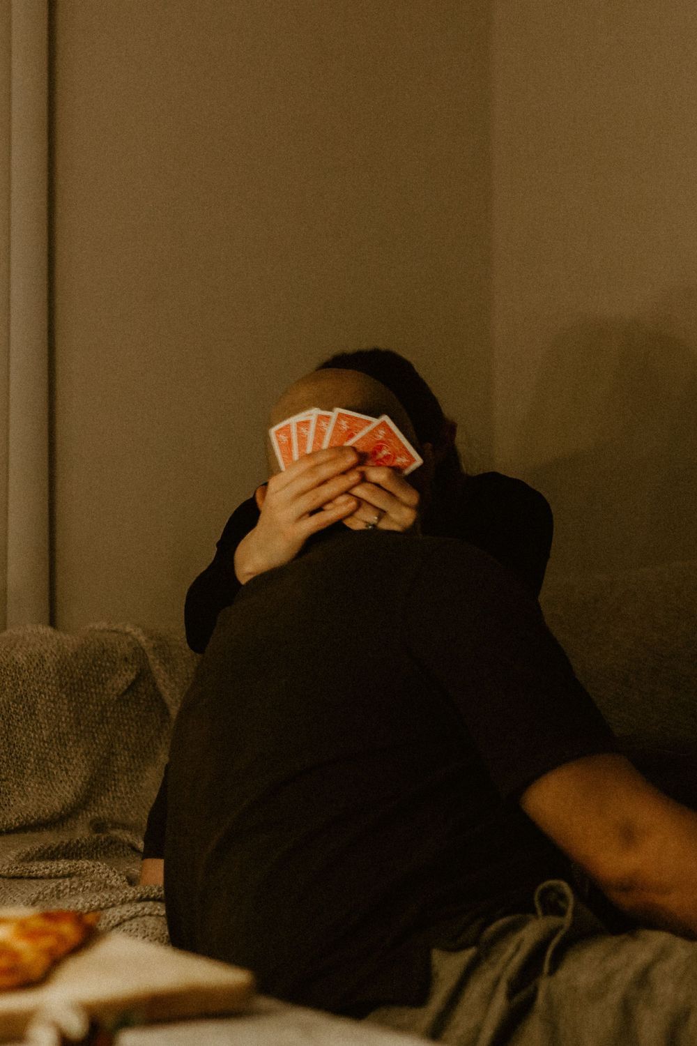 Person holding playing cards while relaxing on a couch in moody lighting.