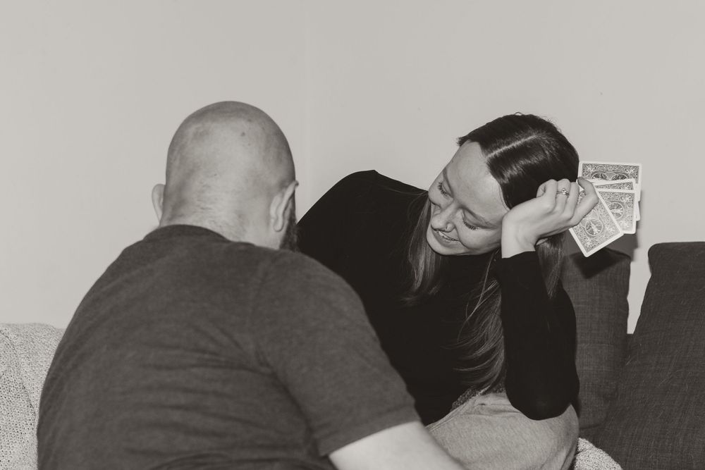 Black and white photo of two people playing cards on couch.