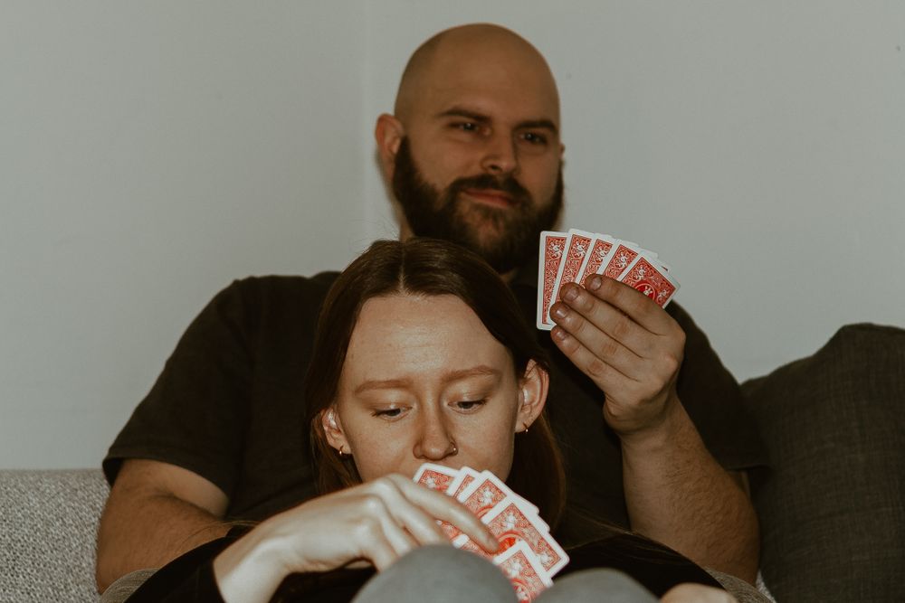 Two people playing card games together on grey couch.