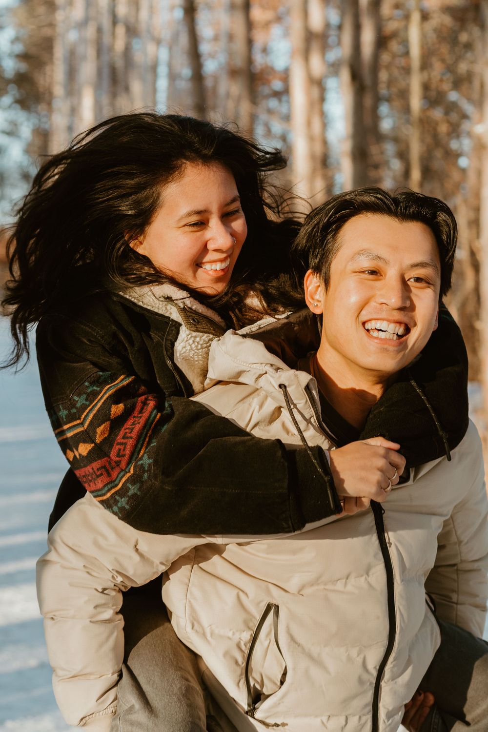 Joyful couple laughing while piggyback riding in snowy winter forest.