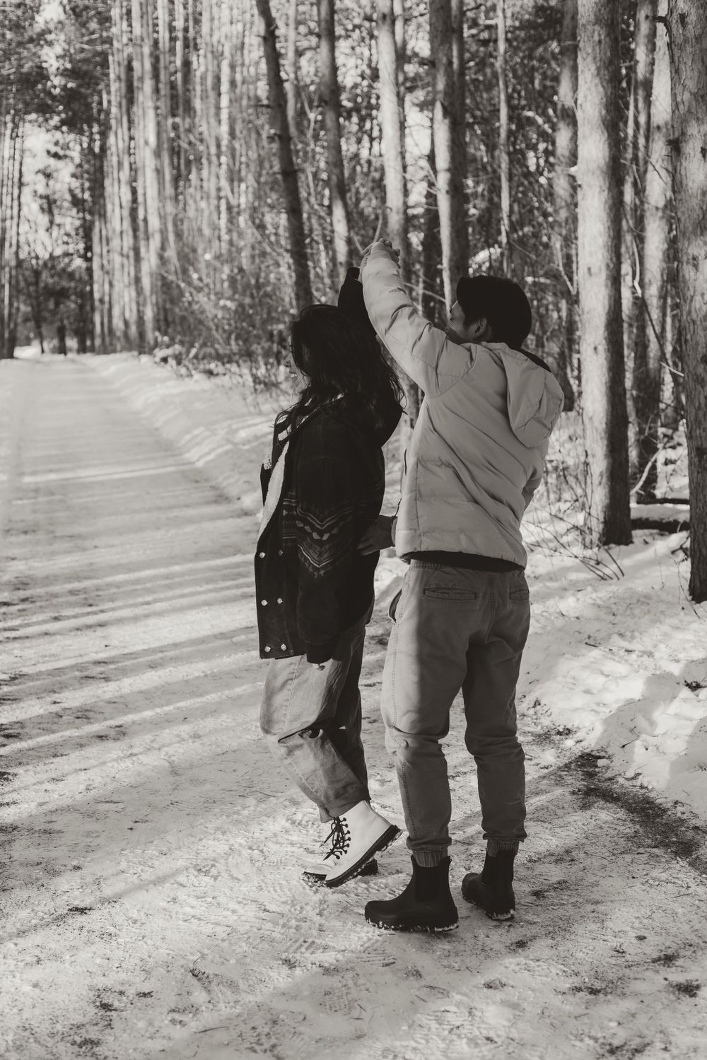 Black and white photo of couple dancing on snowy forest path.