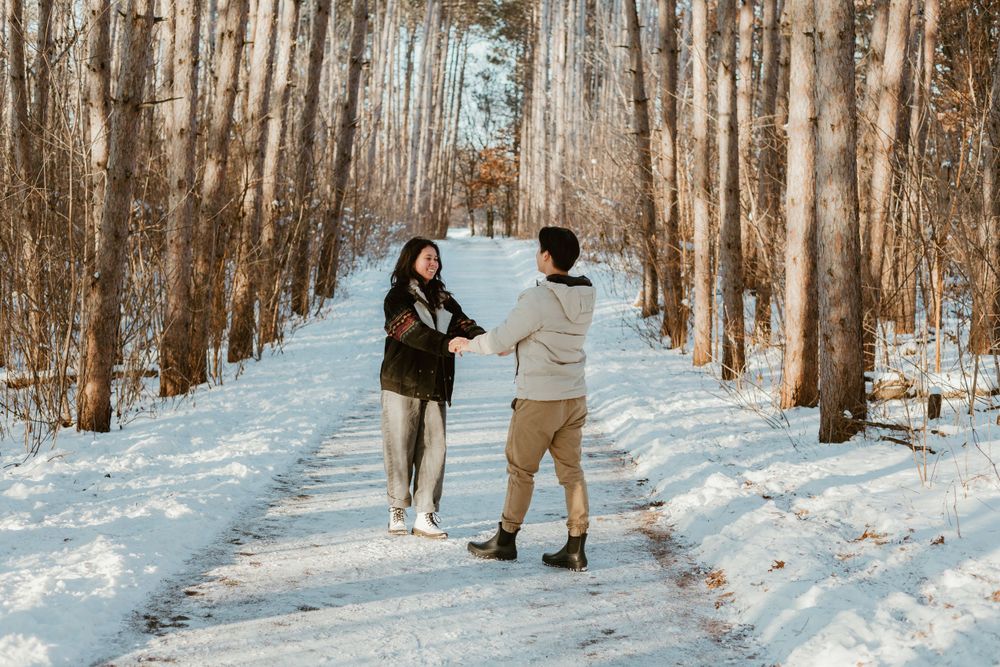 Couple walks hand in hand down snow-covered forest path.