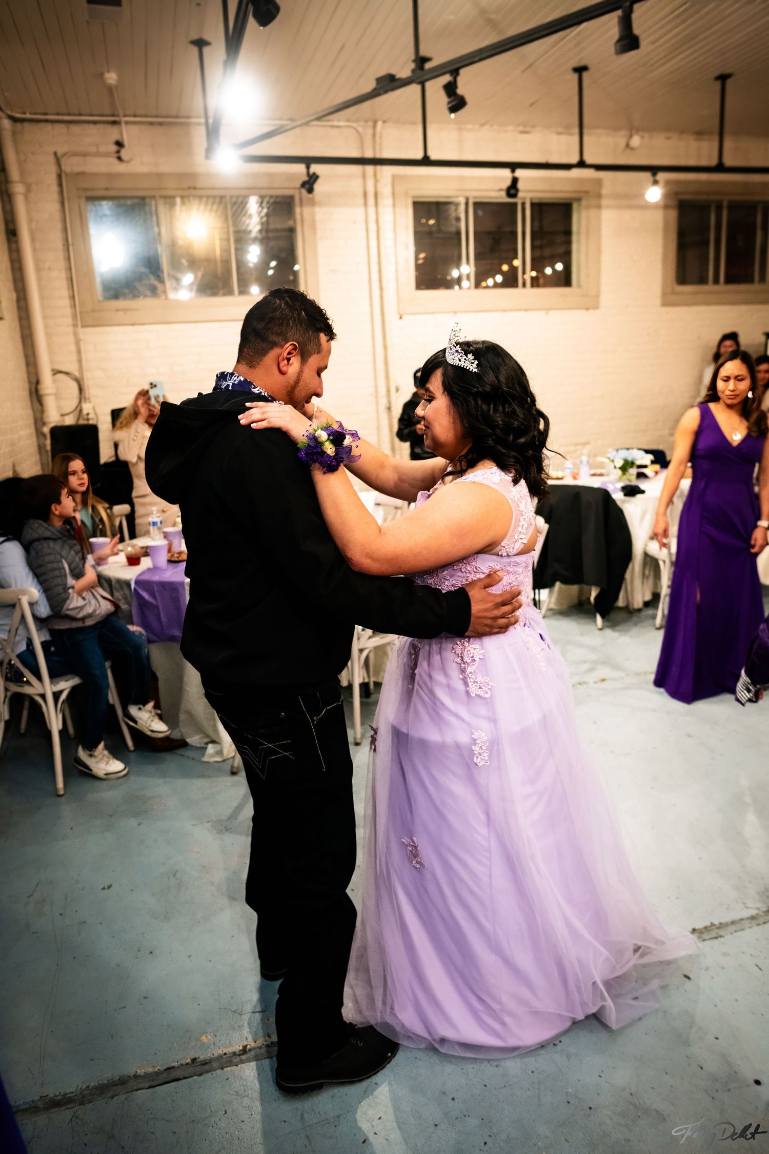 A couple shares a dance at a formal celebration in a decorated venue.