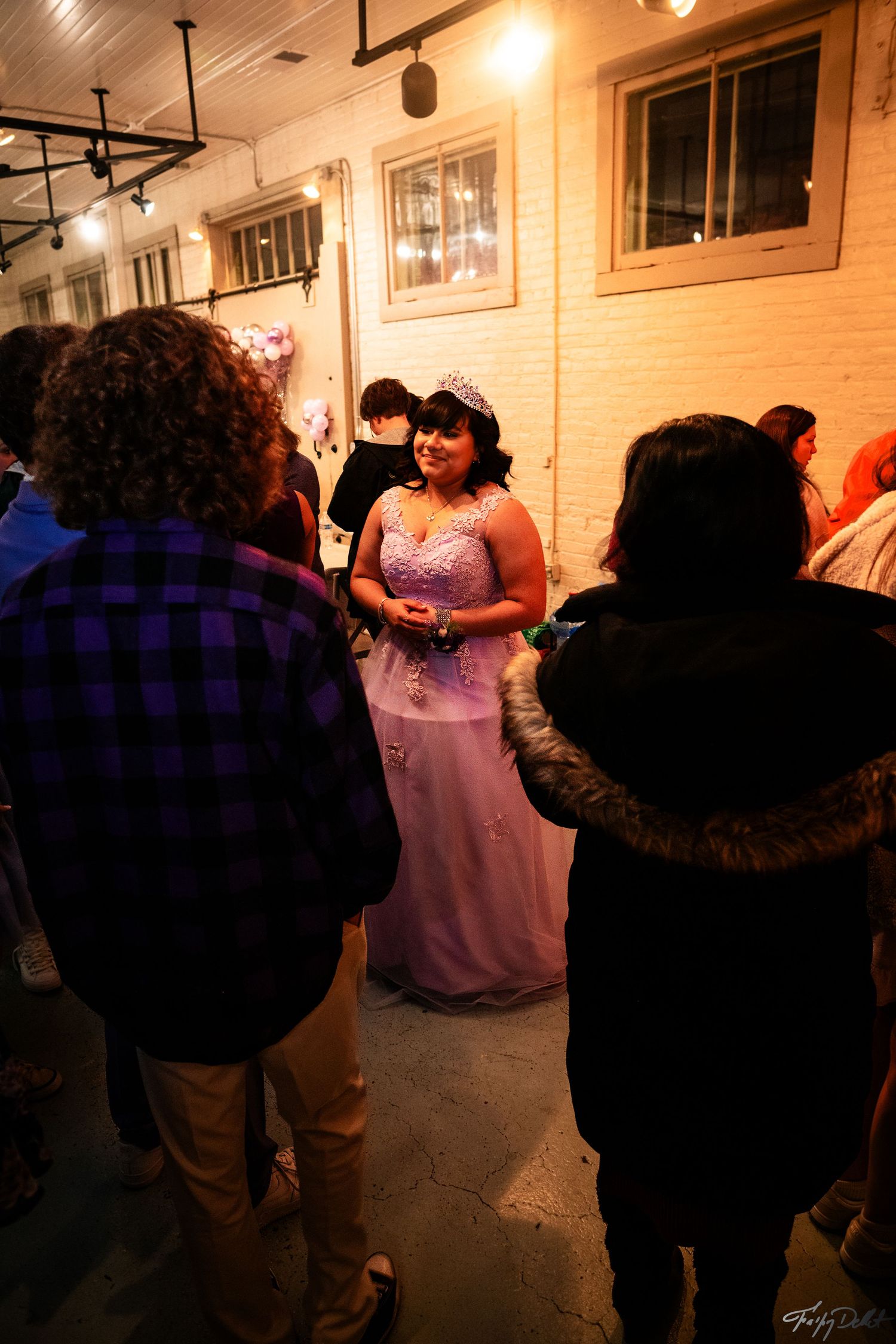 Partygoers mingle at an indoor celebration with warm lighting and brick walls.