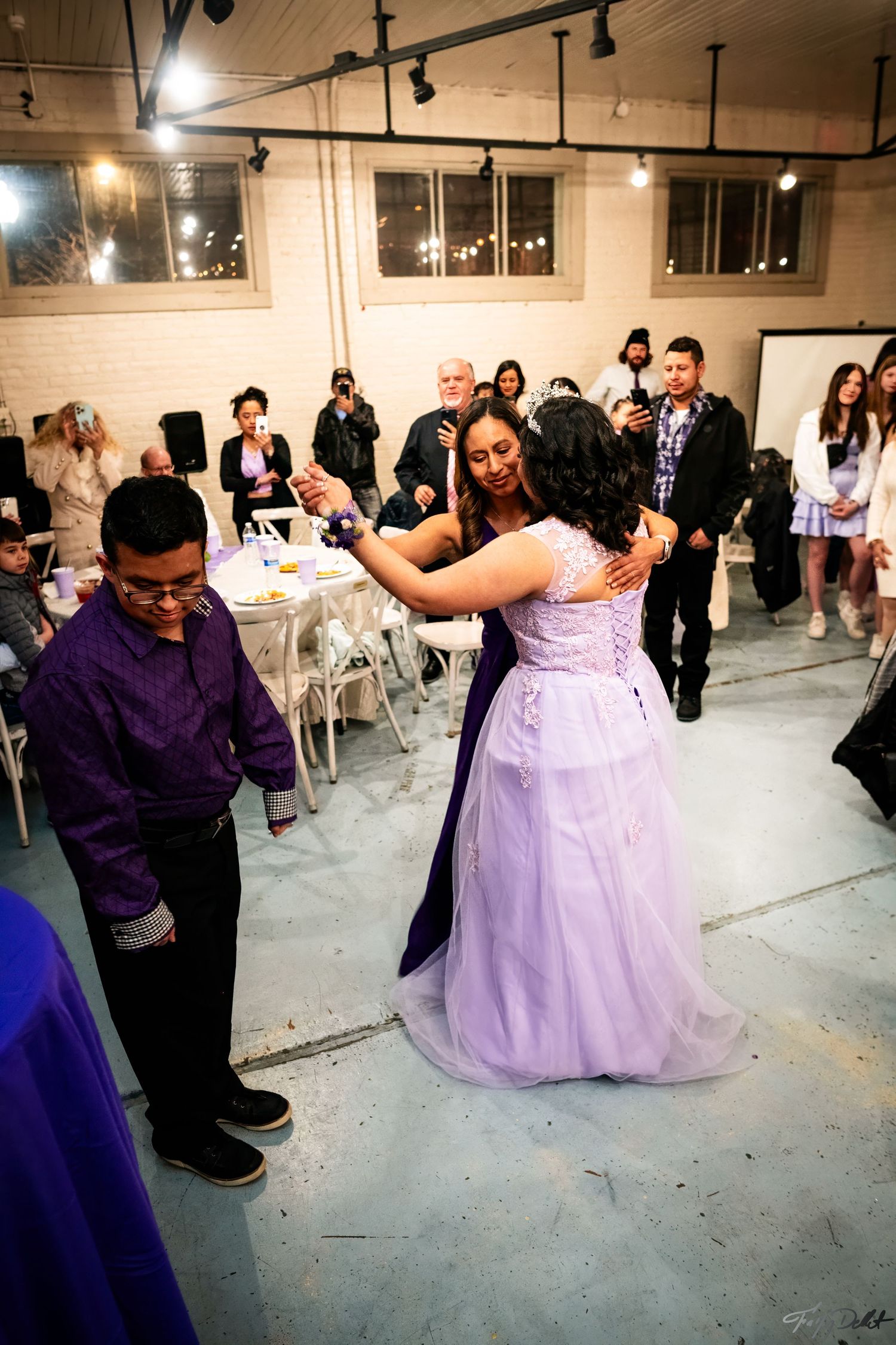Guests dance at a celebration in a venue with industrial-style lighting and brick walls.