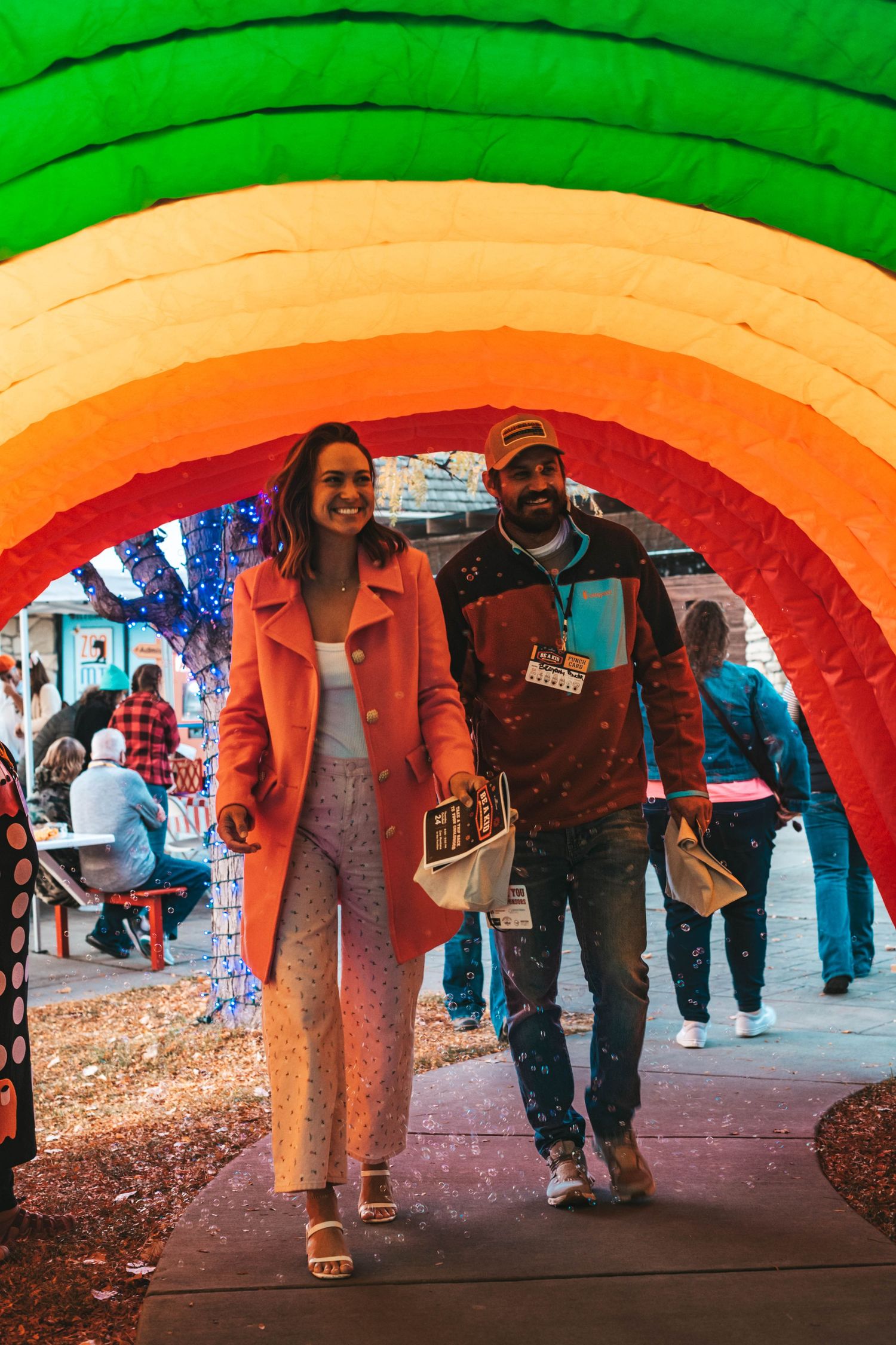 People walking through a colorful rainbow-painted tunnel with changing gradient lighting from green to red.