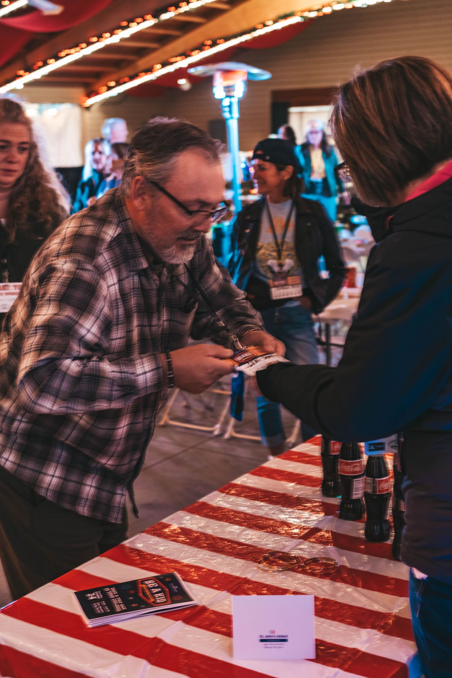 Person signing documents on a red and white striped tablecloth at an indoor event venue.