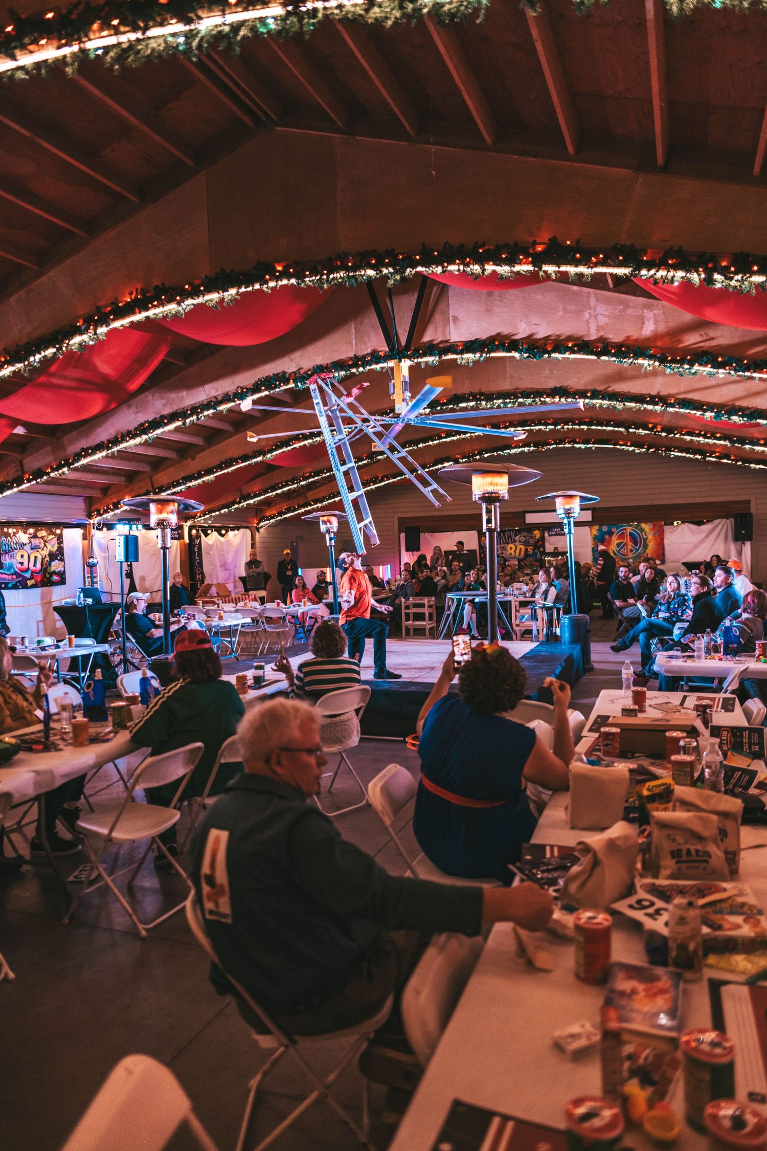 A panoramic view of a dimly lit indoor gathering space decorated with string lights and filled with seated attendees.