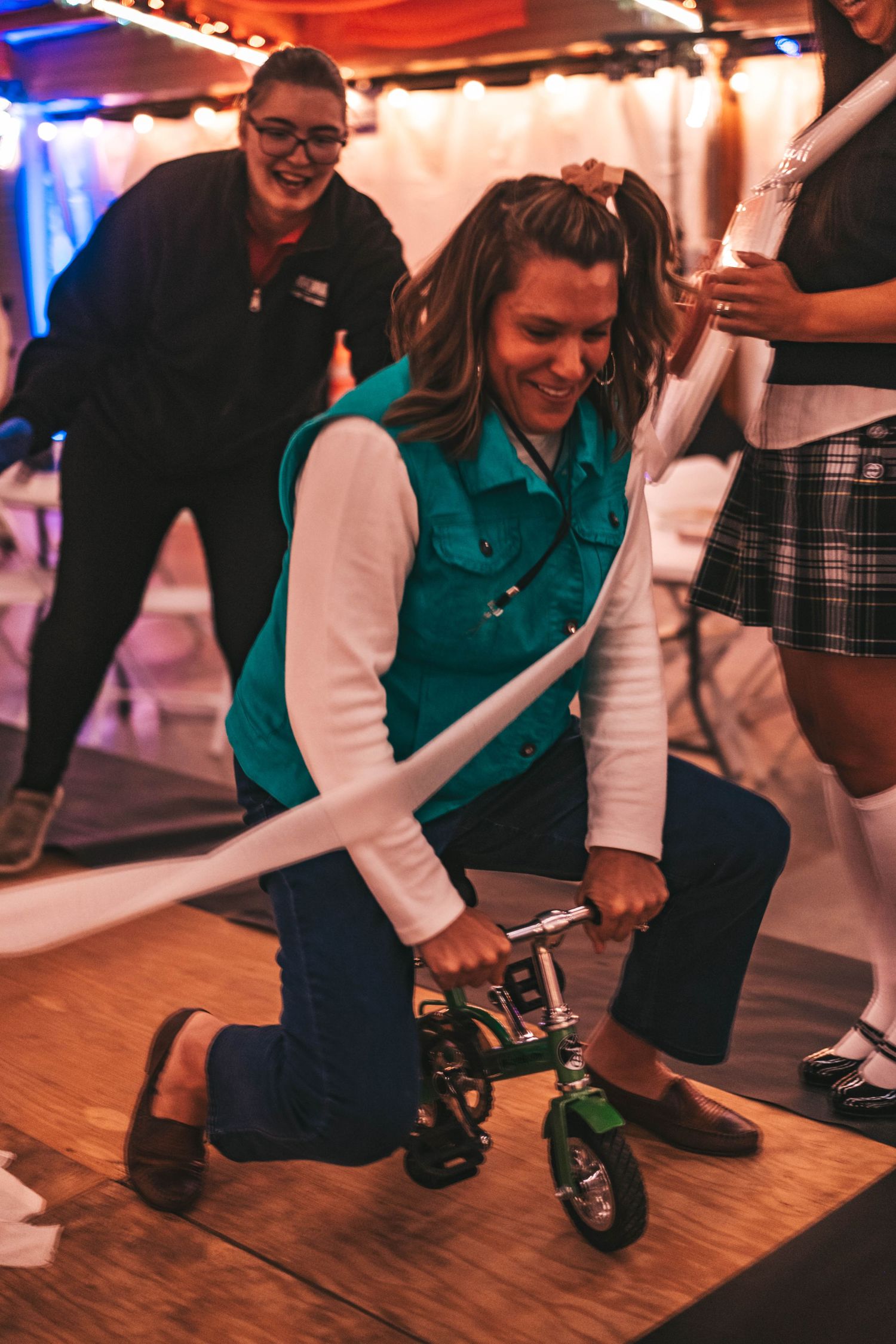 People dancing and having fun on a wooden dance floor at an indoor event with colored lighting.