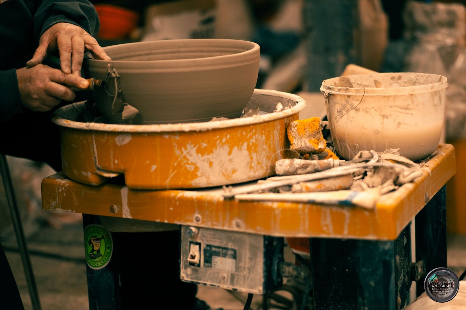 Clay pottery wheel surrounded by crafting tools and orange work surface.