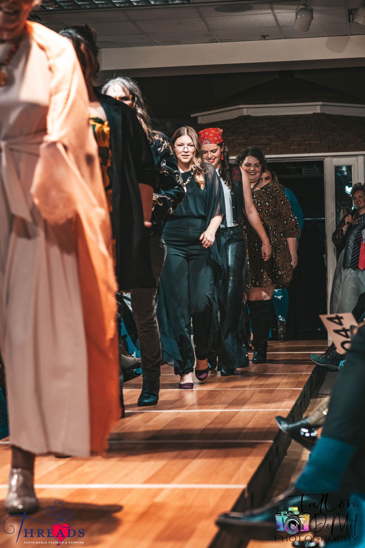 Models walking down catwalk during fashion show with audience seated along sides.