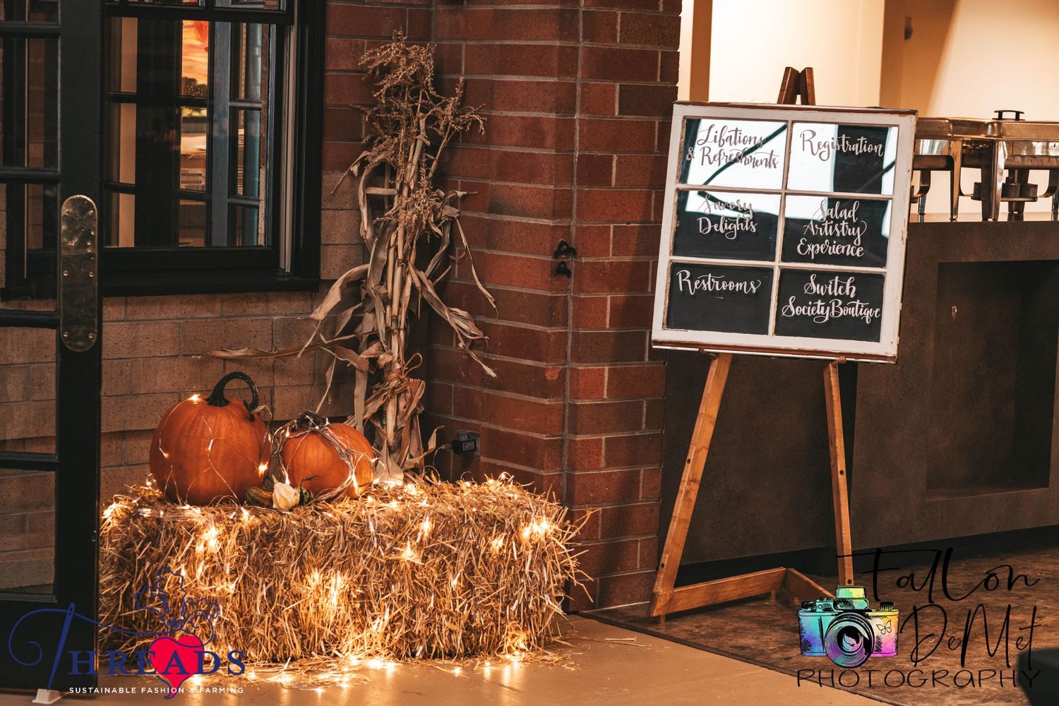 Fall decorative display with pumpkins and hay bales against a brick wall with a chalkboard sign.
