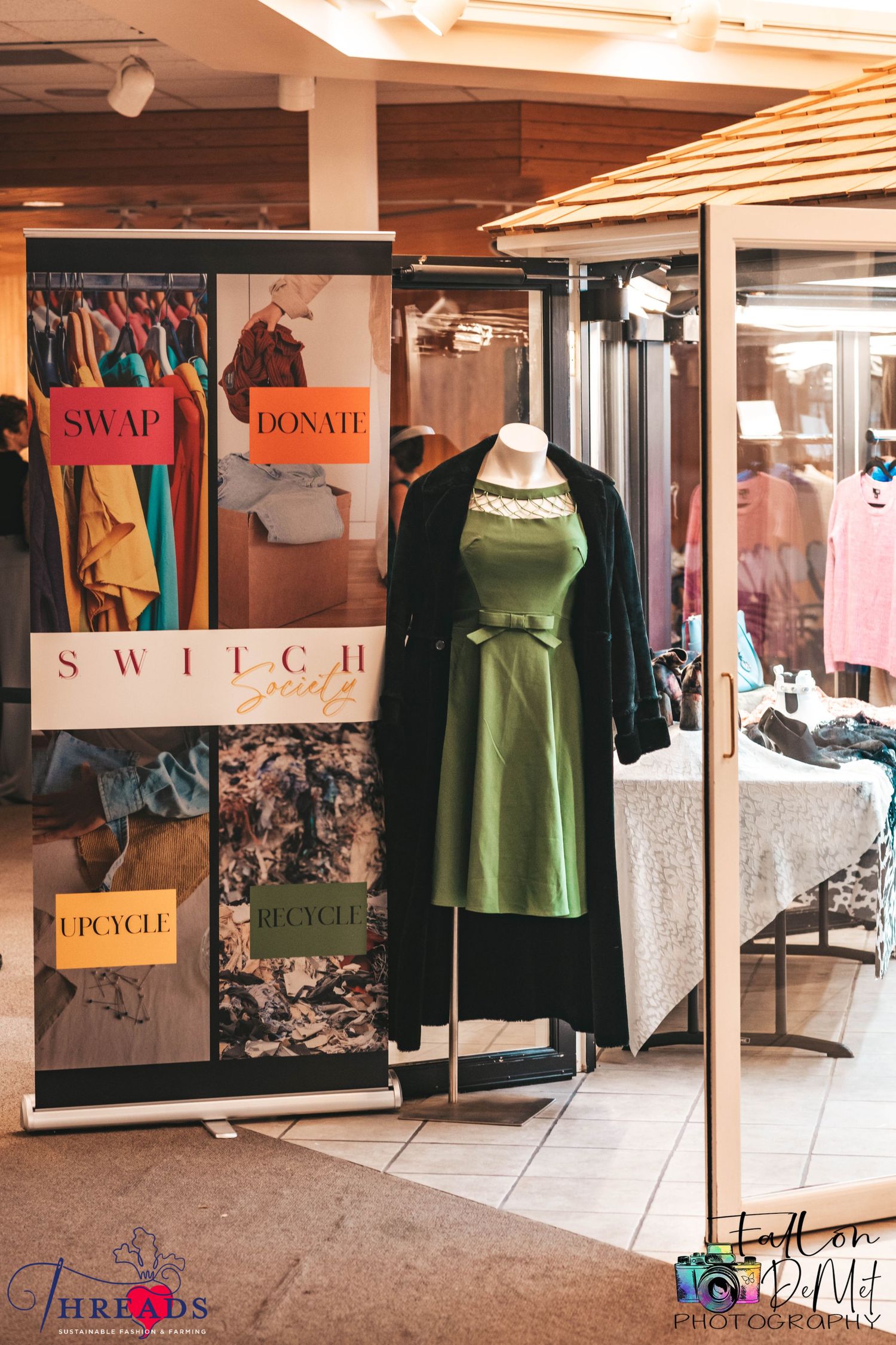 Clothing retail display with green dress and swap/donate signs in a boutique setting.