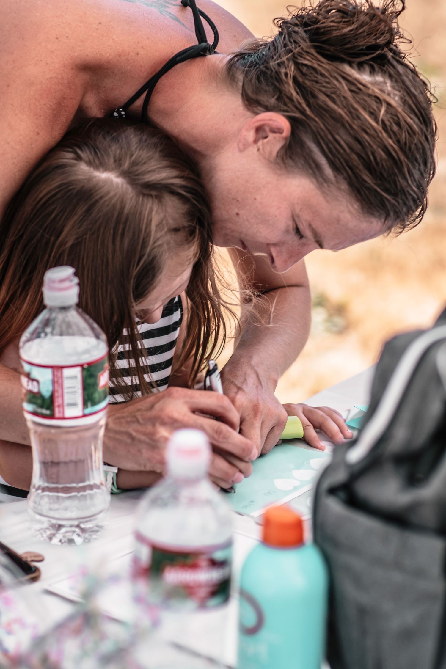 Two people working on a craft project with supplies and water bottle on table.