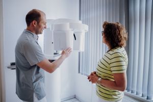 Ein Zahnarzt erklärt eine Patientin die Funktion des Röntgengerätes und zeigt dabei auf den Apparat.