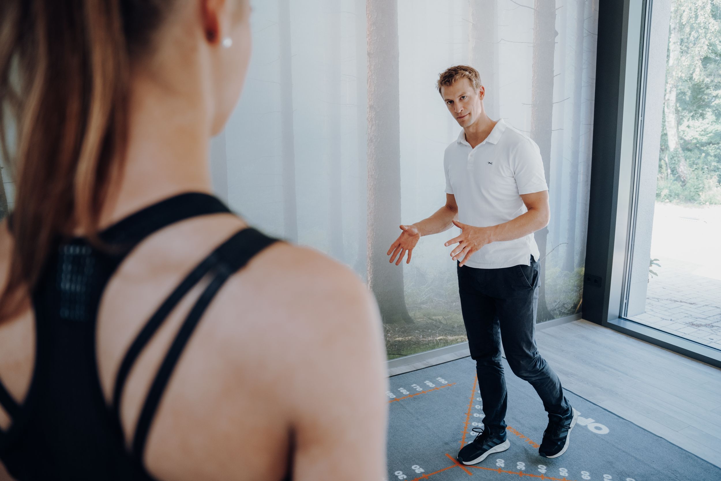 Ein Fitnesscoach erklärt mit seinen Händen und schaut dabei auf die Sportleerin vor ihm. Sie stehen im Fitnessraum von der Funktionellen Chi