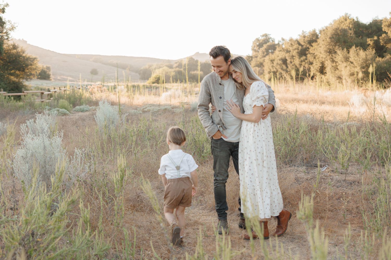 A family enjoys a golden sunset in a rural field with mountains in the distance.
