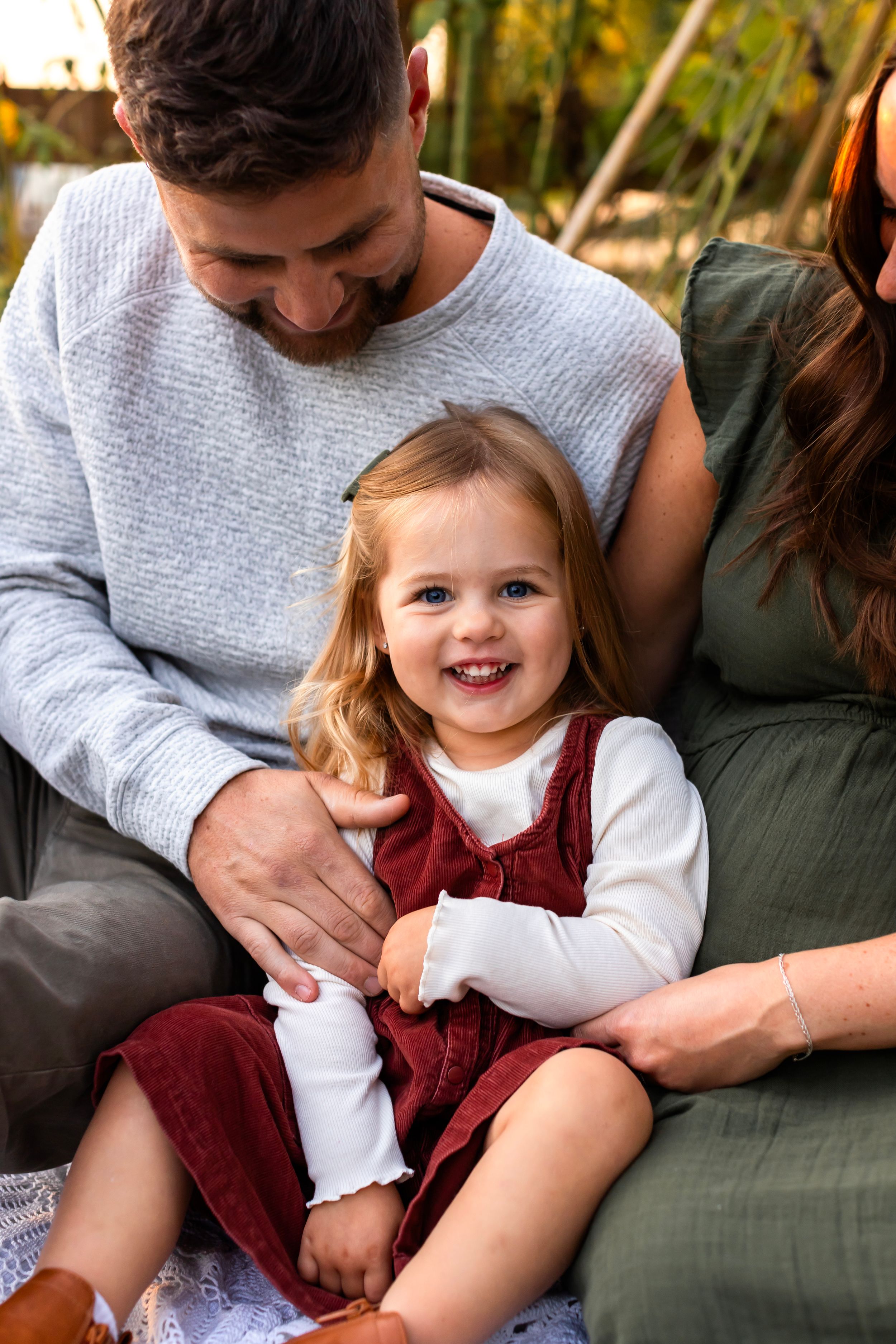 Family moment captured on white blanket with child in burgundy dress.