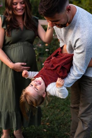 A candid family moment in a garden showing playful interaction with a child being held upside down.