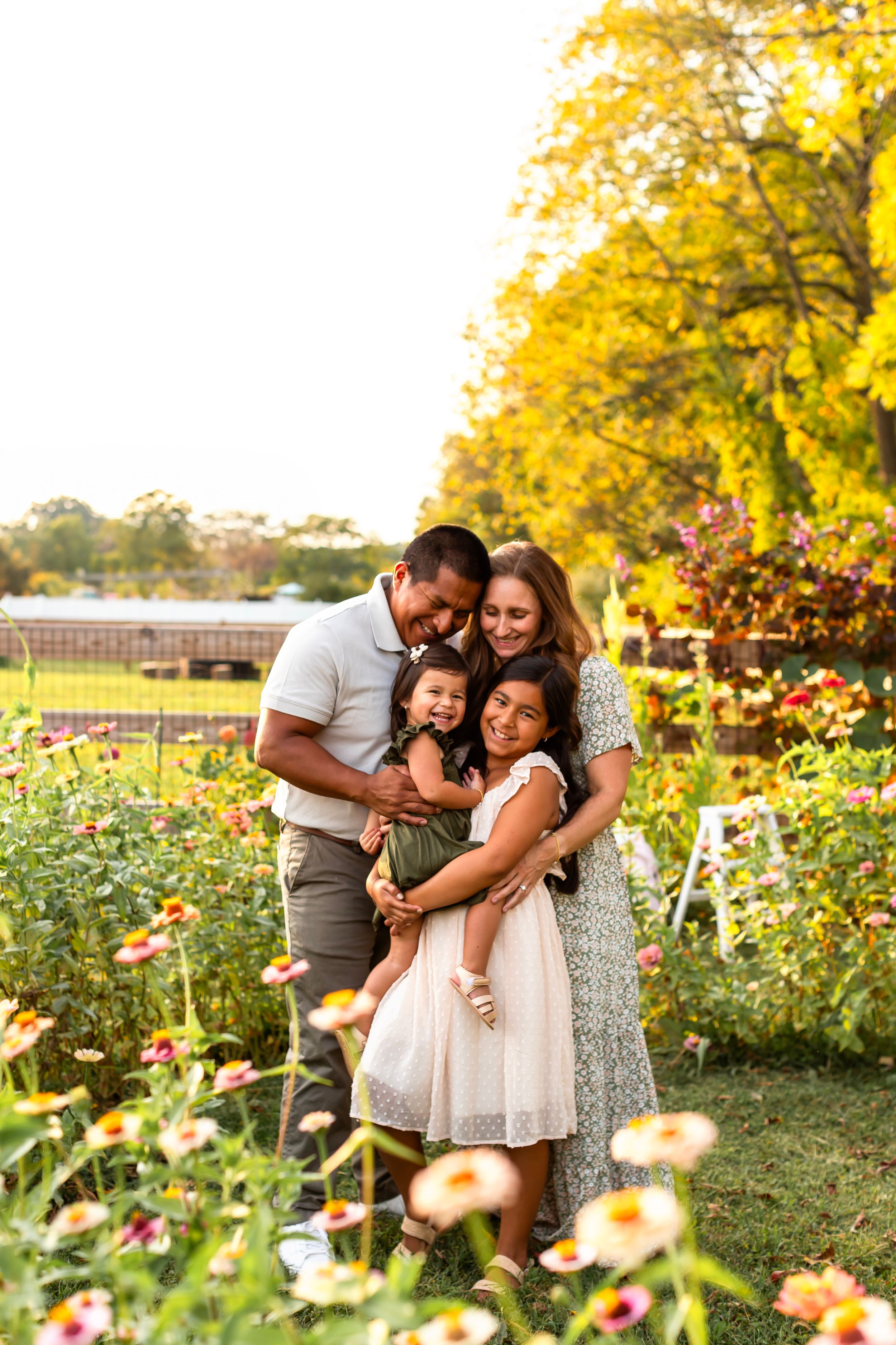 Happy family embracing in flower garden with golden autumn trees in background.