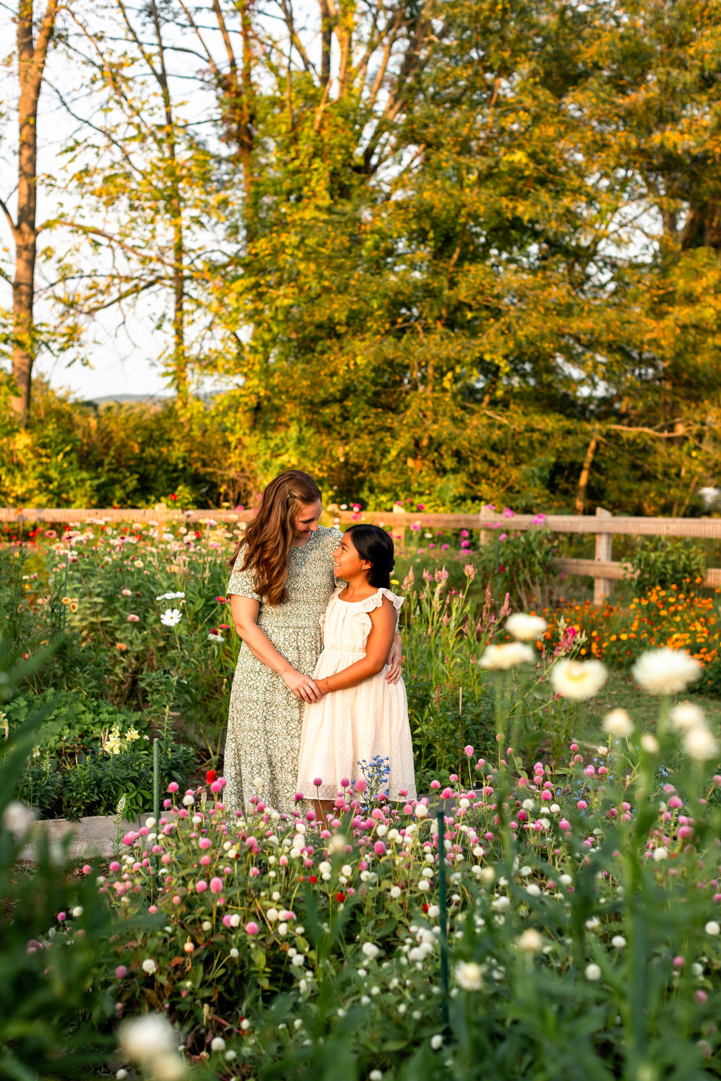 Two people sharing tender moment among pink wildflowers in garden at sunset.