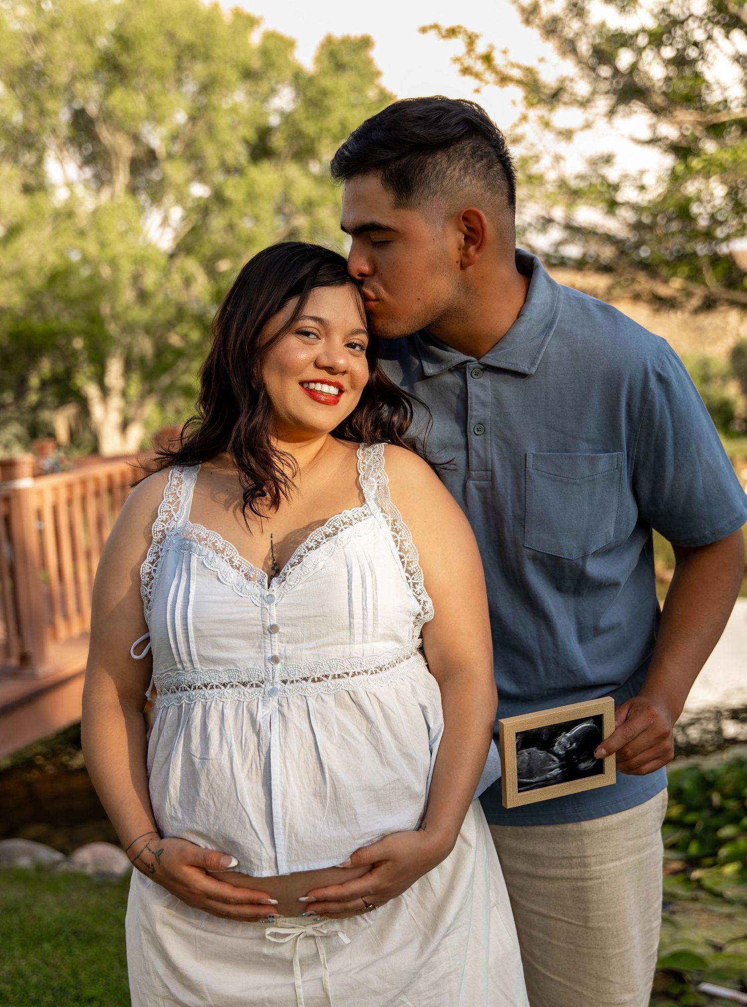 A couple shares an intimate moment outdoors as they hold a sonogram photo during a maternity photo session.