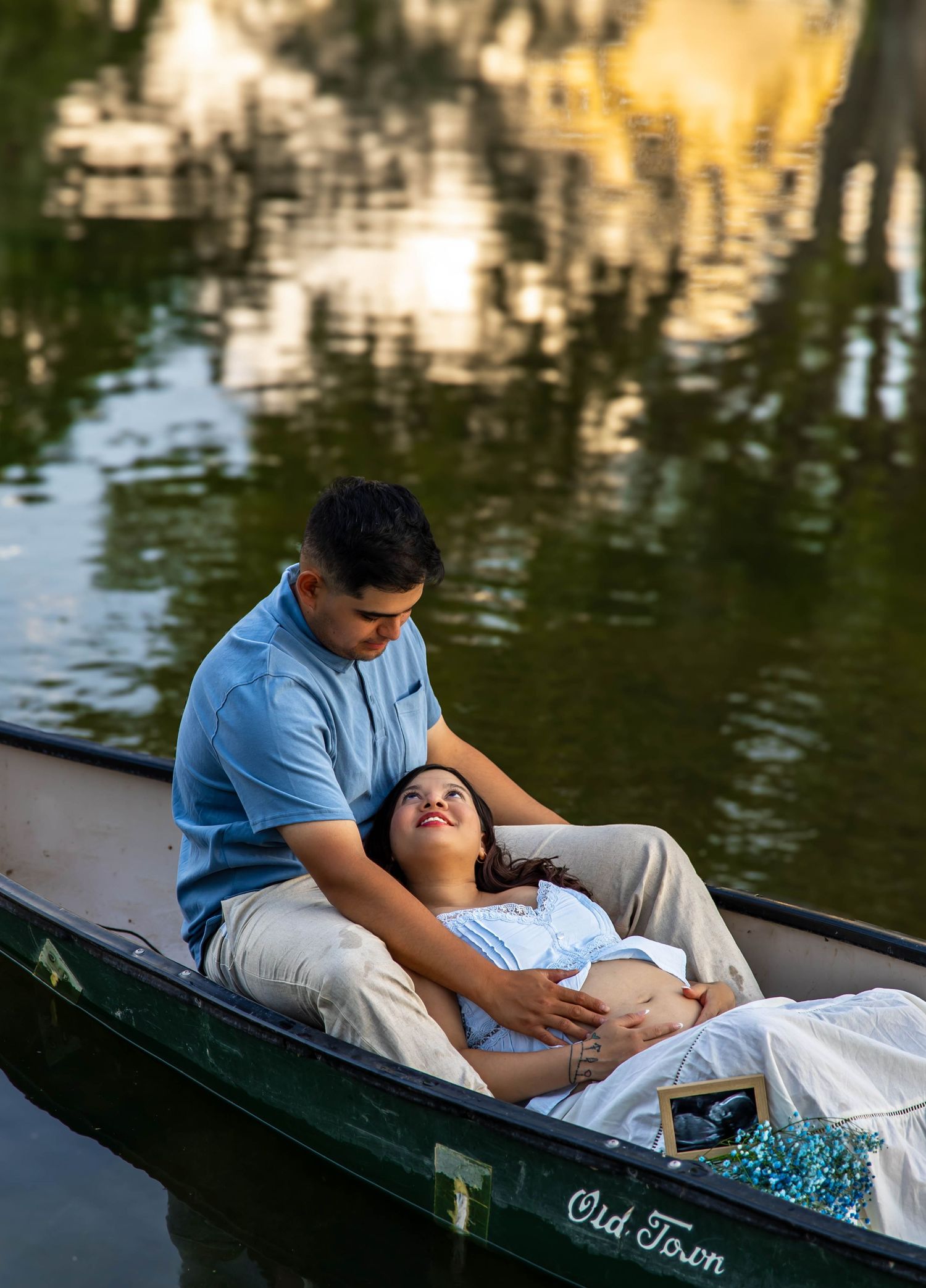 A couple shares a romantic moment while relaxing in a wooden boat on a tranquil lake during sunset.