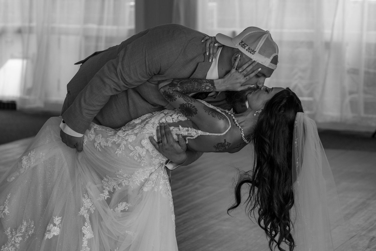 Black and white photo of couple walking through mountain meadow with flowing dress veil.