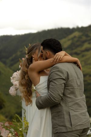 Newlyweds share an intimate moment against a backdrop of lush mountains in Hawaii.