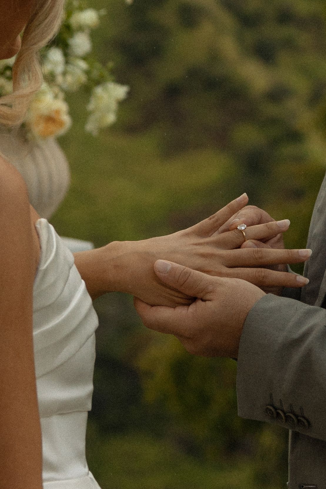 Close-up of hands exchanging wedding rings during an outdoor ceremony.