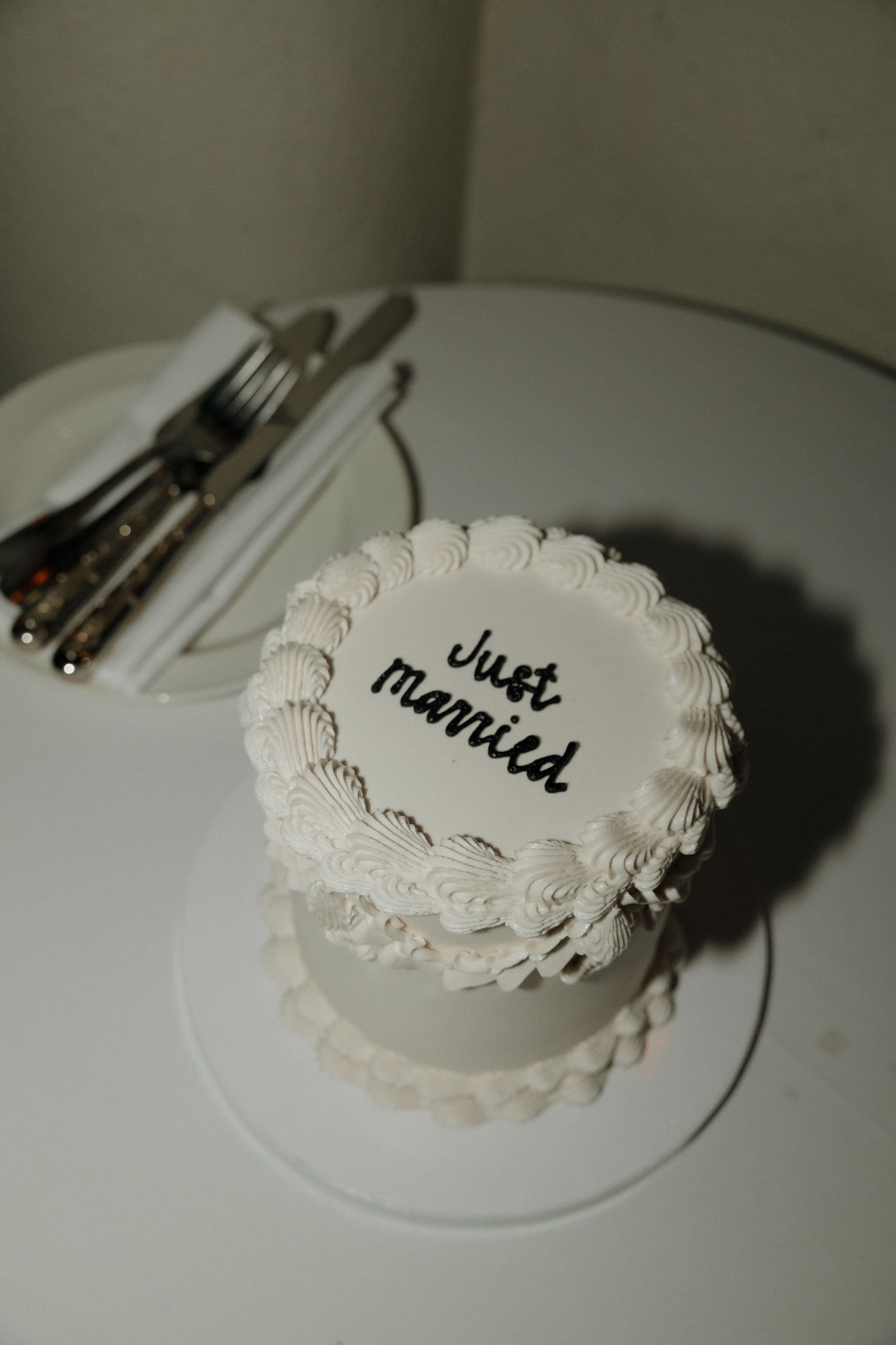 A small, white, vintage inspired wedding cake with 'Just Married' written in black script.