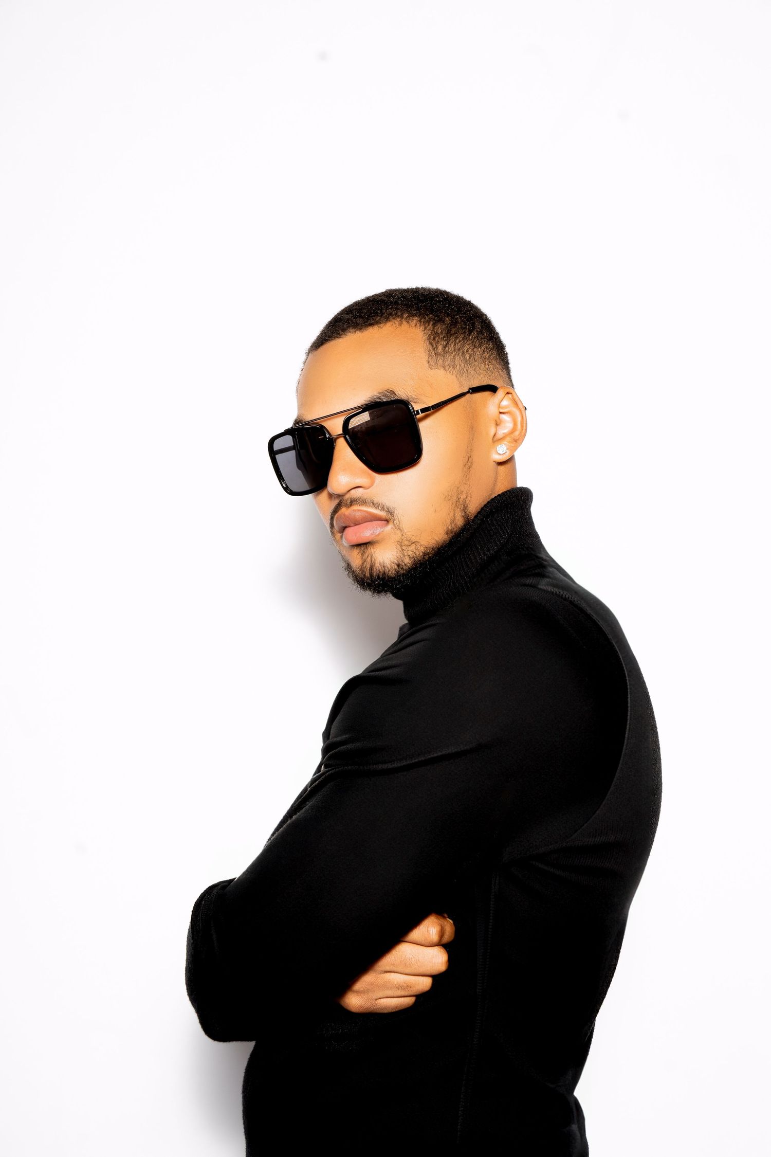 Fashion portrait of person in black turtleneck and sunglasses against white background.