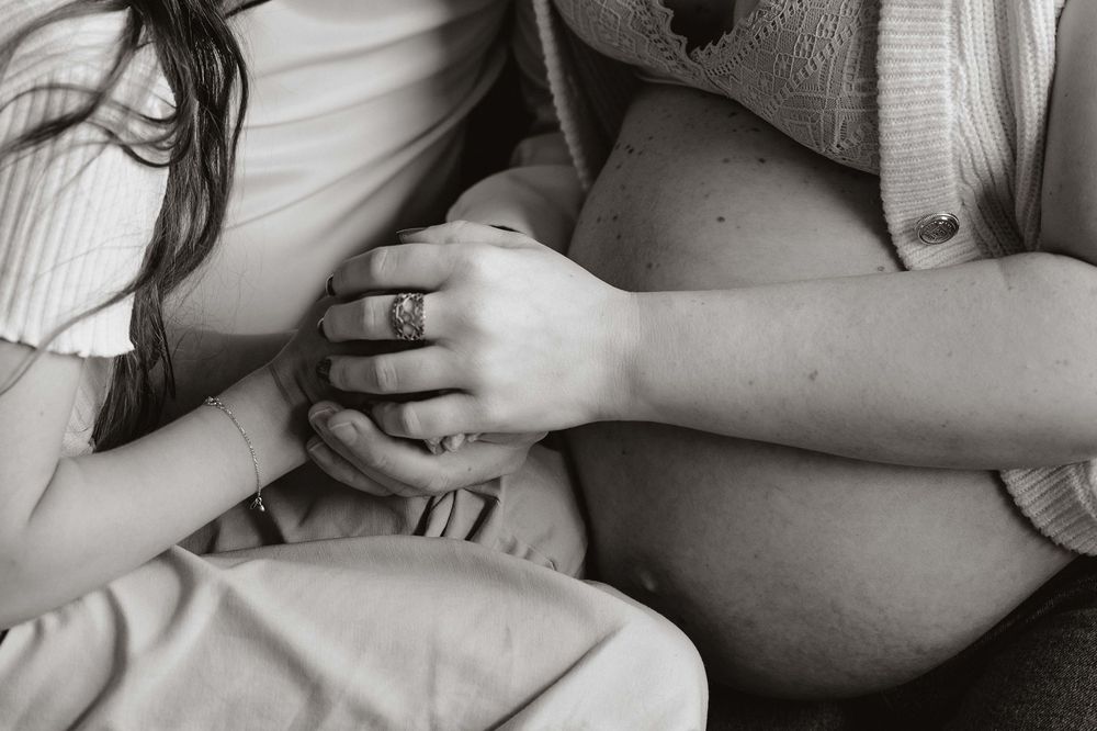 Black and white photo of a pregnant woman with a child's hand resting on her baby bump.