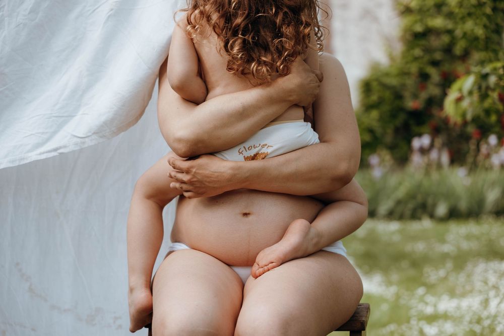 Close up artistic photo of a person embracing themselves against a white sheet in a garden setting.