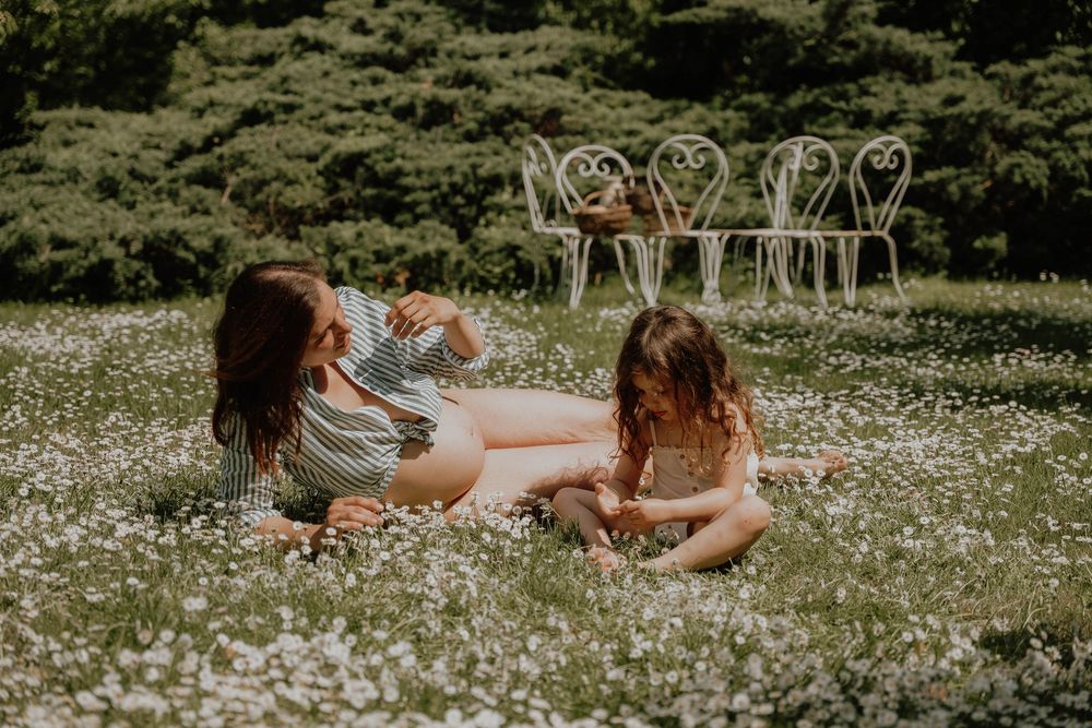 Two girls sitting in a field of white wildflowers with ornate white chairs in the background.