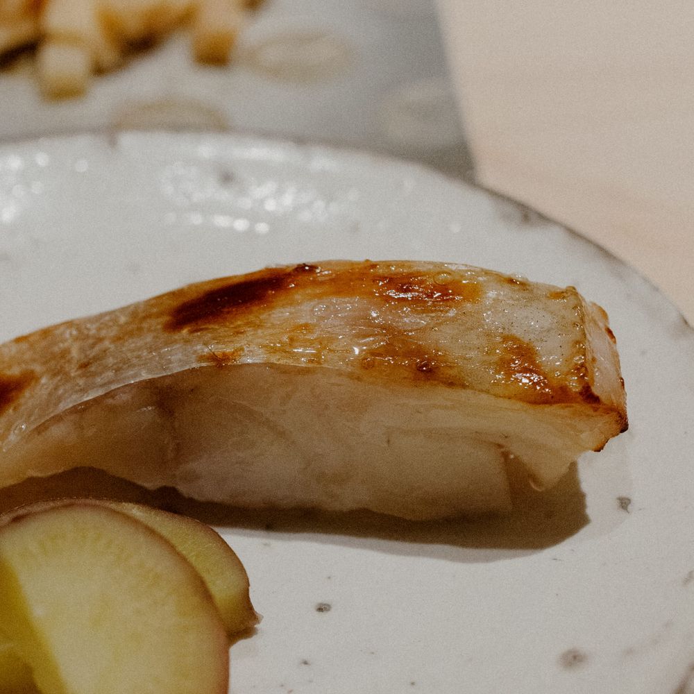 Grilled white fish fillet served with a lemon slice on a ceramic plate.