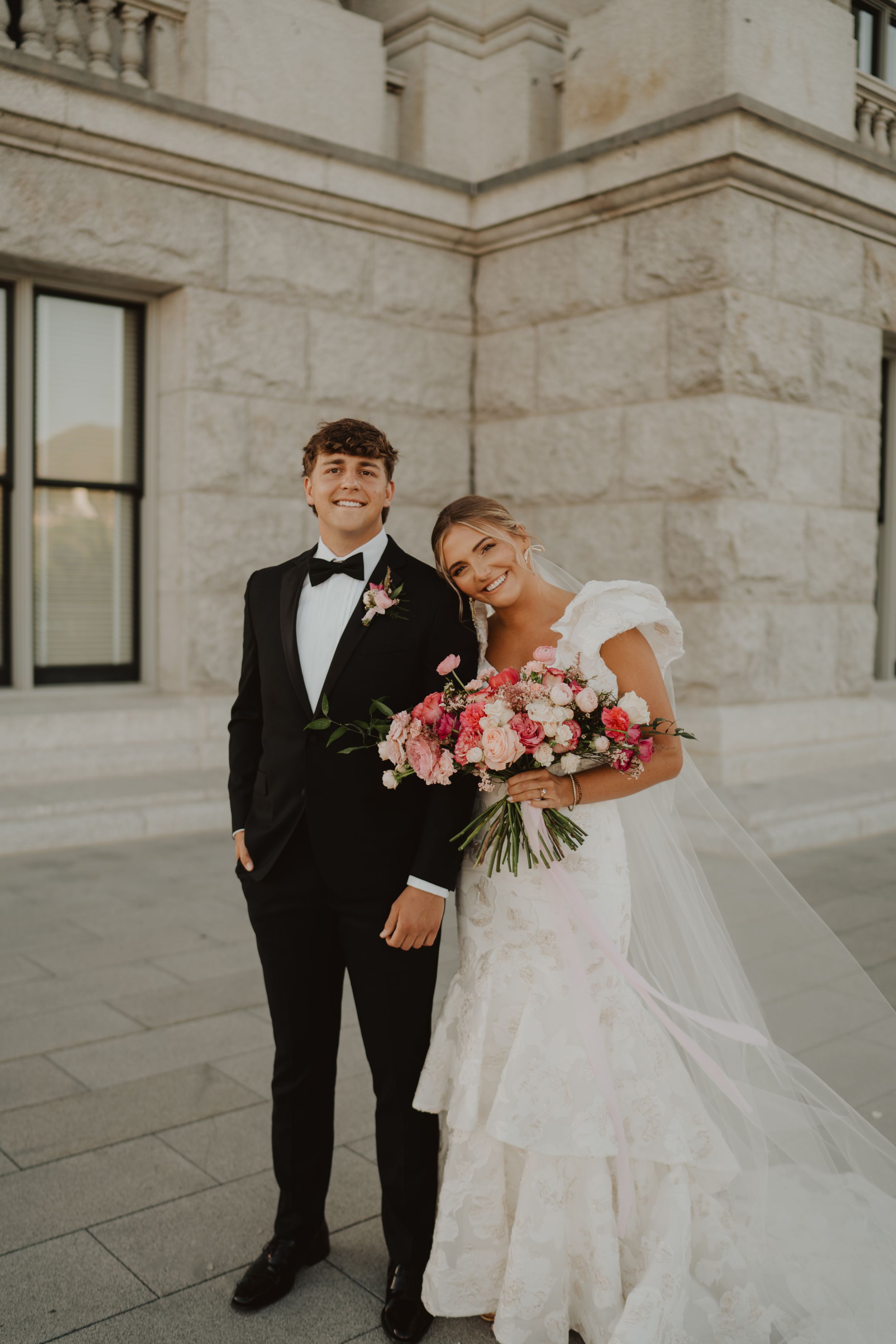 Wedding party poses playfully outside a grand stone building.