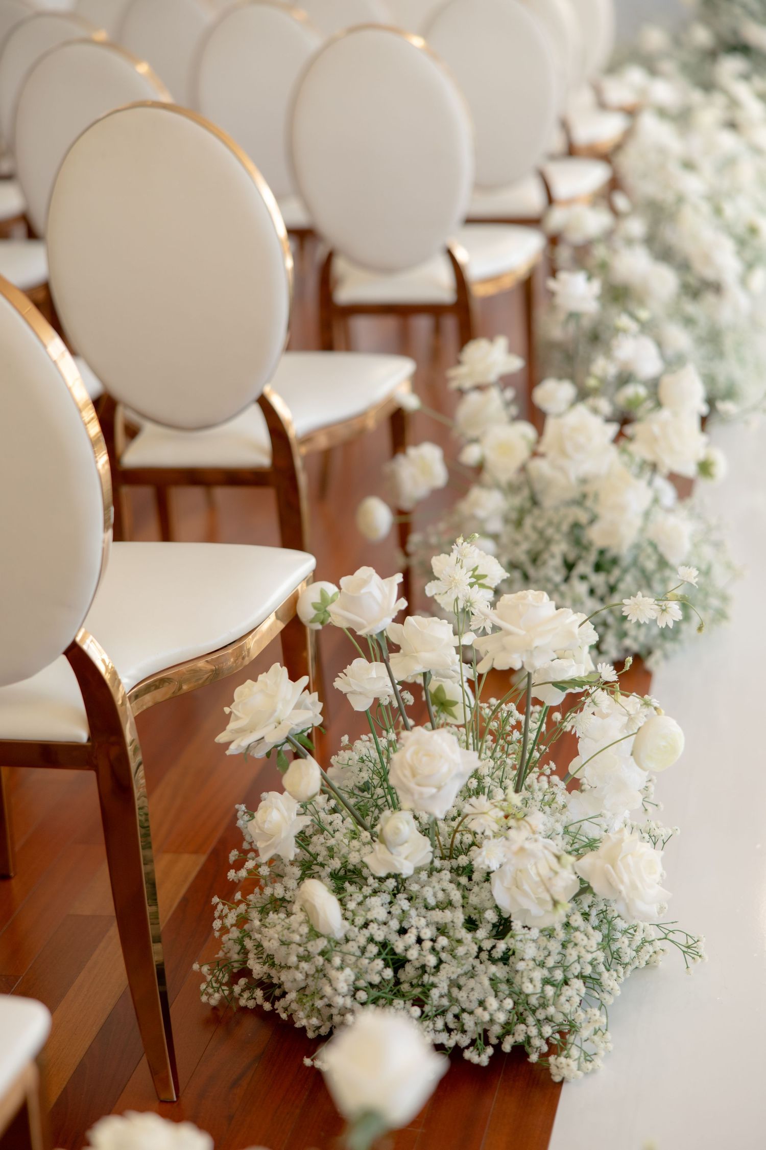 Close-up of white roses and baby's breath floral arrangements along elegant white ceremony chairs.