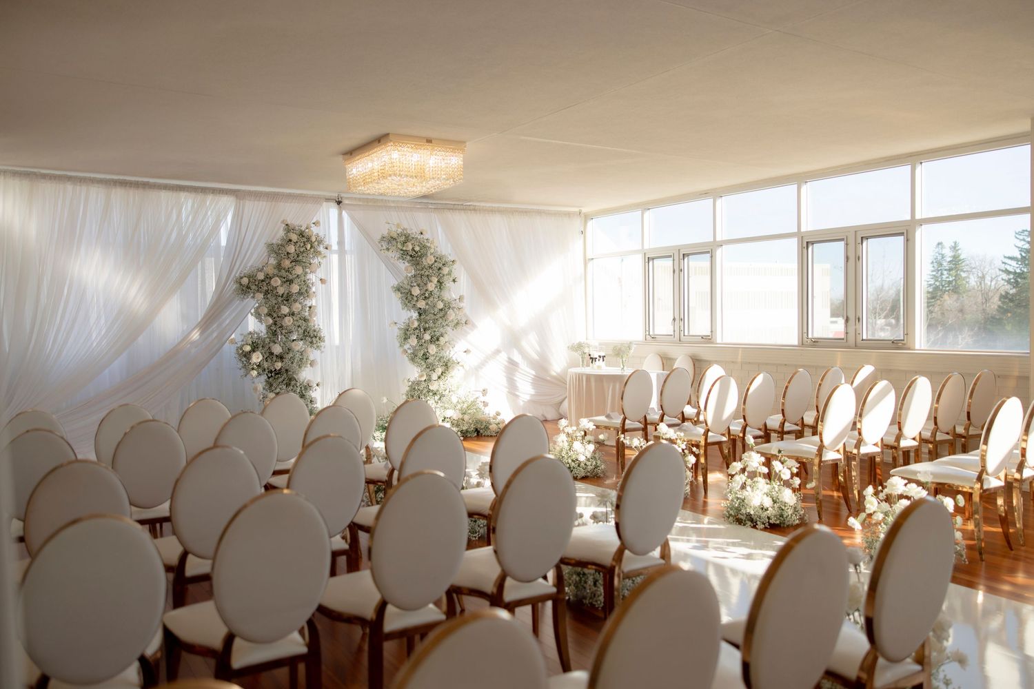 Bright wedding venue with white chairs and floral decorations bathed in natural sunlight.