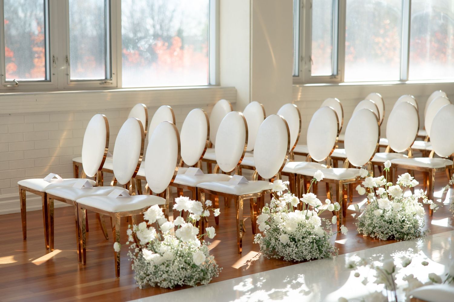 White ceremony chairs arranged in rows with floral arrangements and sunlight streaming through windows.