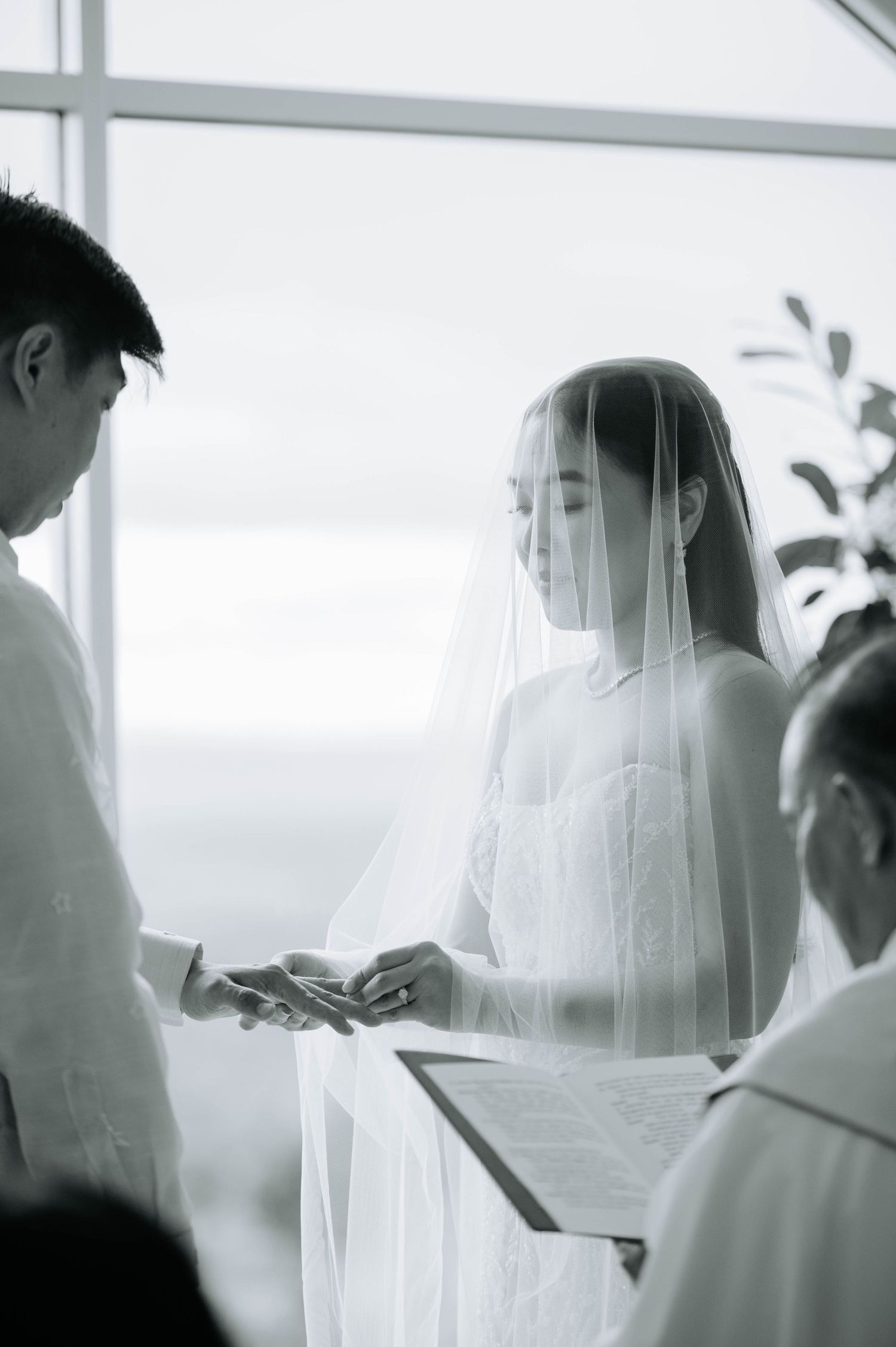 An intimate wedding ceremony moment captured in black and white by large windows.